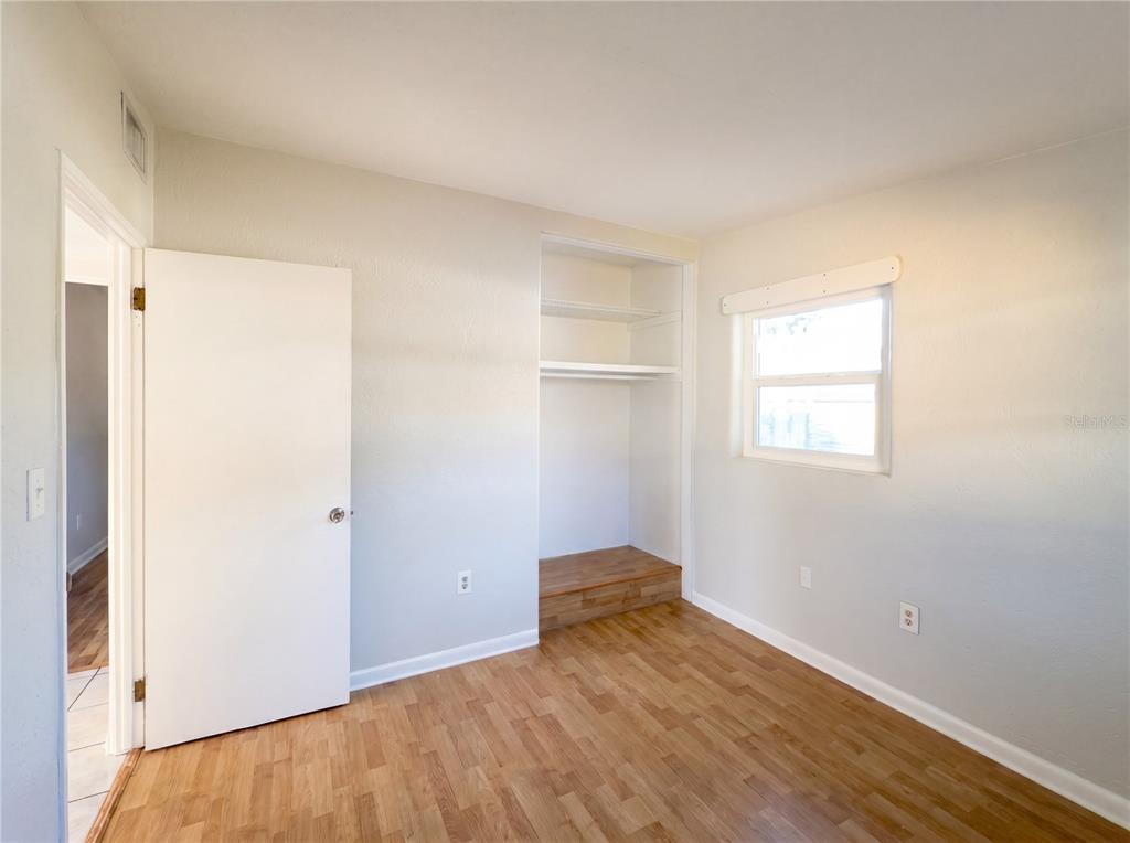 An empty bedroom features light gray walls, hardwood floors, a white door, and built-in shelving — 911 NEW YORK STREET, EDGEWATER, FL