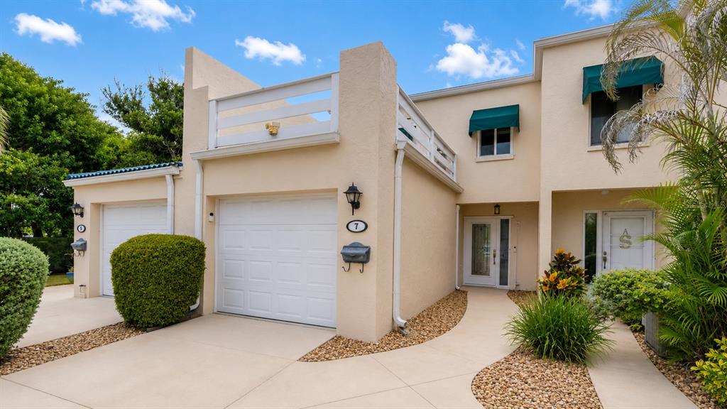 A two-story stucco townhouse features a garage, a balcony, and a landscaped front walkway — 7 EMERALD COURT, SATELLITE BEACH, FL