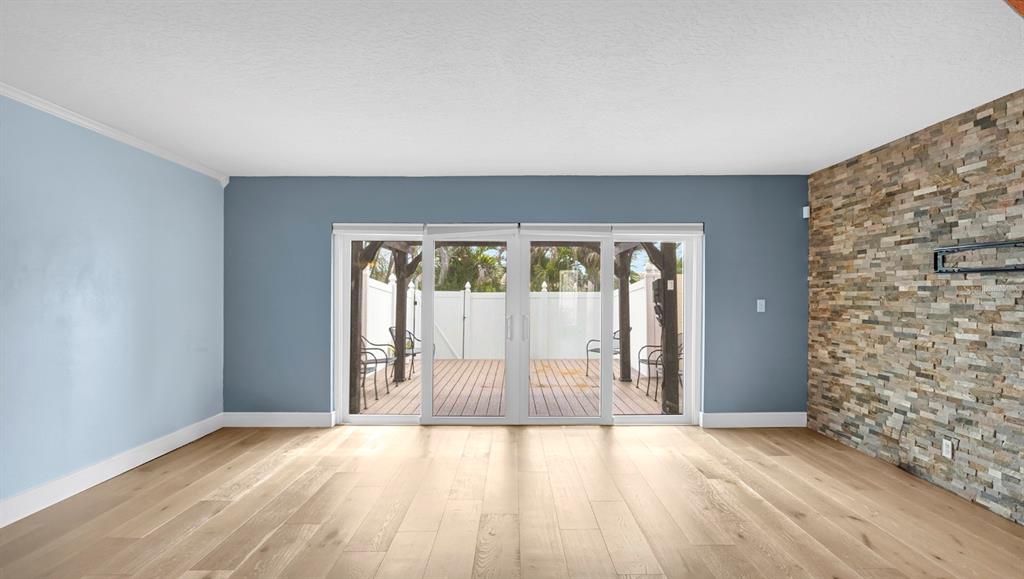 An empty living room features light wood flooring, blue walls, and a stone accent wall — 7 EMERALD COURT, SATELLITE BEACH, FL