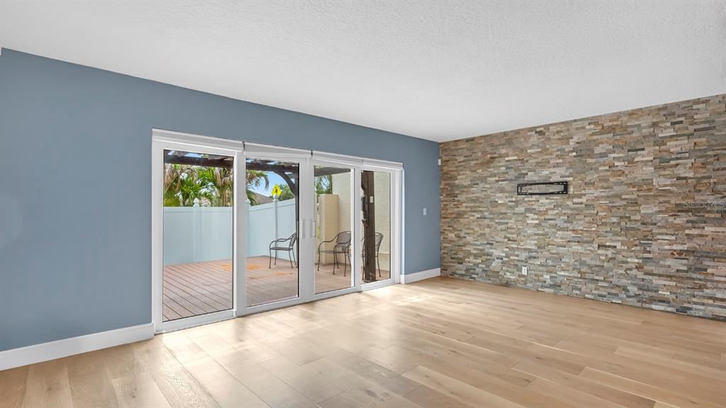 A room with light wood floors, a stone accent wall, and sliding glass doors to a deck — 7 EMERALD COURT, SATELLITE BEACH, FL