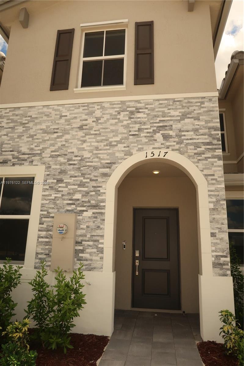 A two-story house exterior features a stone veneer facade, an arched entryway, and a dark door — 1517 SE 27th Rd, Homestead FL 33035, HOMESTEAD, FL