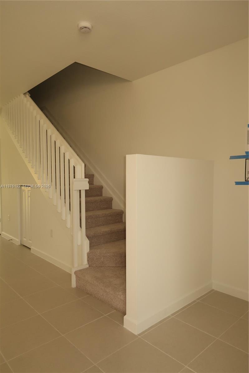 A carpeted staircase with a white railing leads upward in a room with tiled floors — 1517 SE 27th Rd, Homestead FL 33035, HOMESTEAD, FL