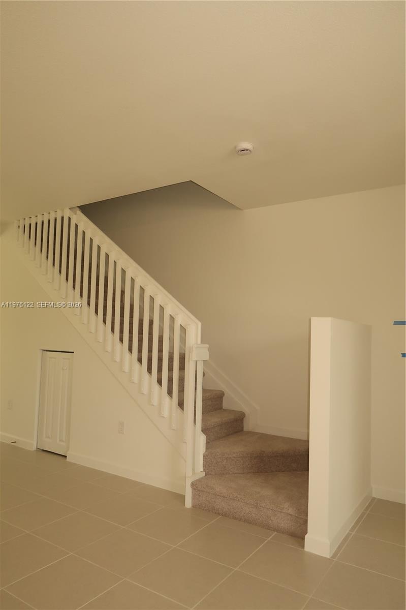 A staircase with a white wooden railing leads to an upper level in a room — 1517 SE 27th Rd, Homestead FL 33035, HOMESTEAD, FL