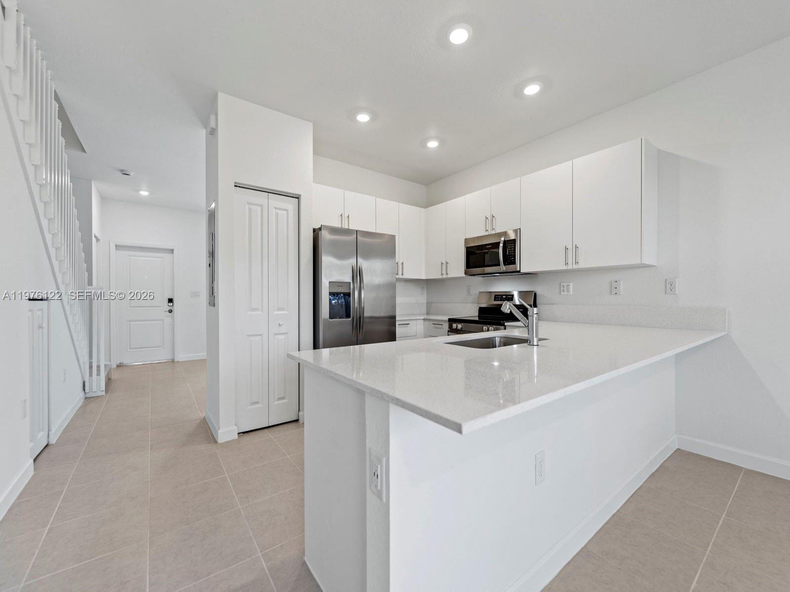 A modern kitchen features white cabinets, stainless steel appliances, and a quartz-topped island — 1517 SE 27th Rd, Homestead FL 33035, HOMESTEAD, FL
