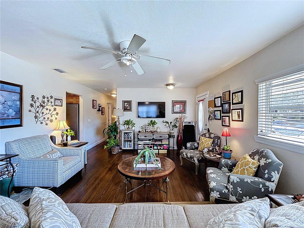 A living room with hardwood floors, a sofa, armchairs, and an open doorway to a kitchen — 717 W END CRESCENT N, LAKELAND, FL