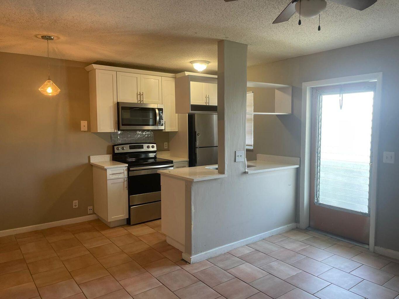 A kitchen with white cabinets, stainless steel appliances, and tile flooring, featuring a breakfast bar — 702 N L Street # 13, FL 33460, FL