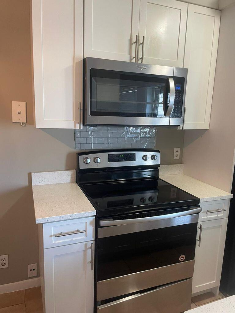 A kitchen features white cabinets, a stainless steel microwave, a black range, and light countertops — 702 N L Street # 13, FL 33460, FL