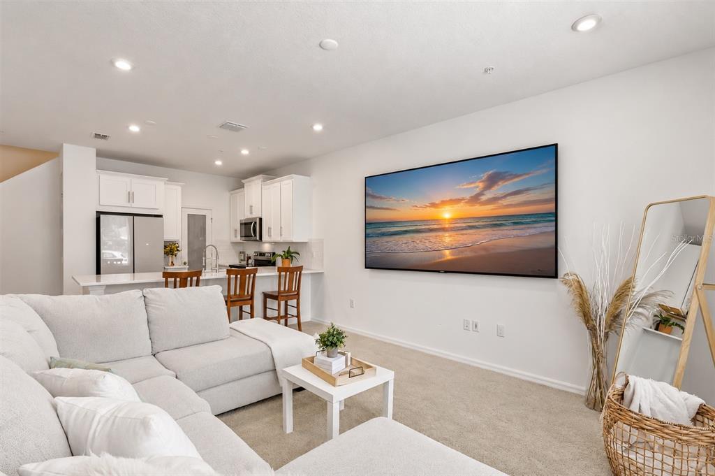 A living room with a large wall-mounted television, a sectional sofa, and an open kitchen — 10245 HIGHLINE CREST STREET, ORLANDO, FL