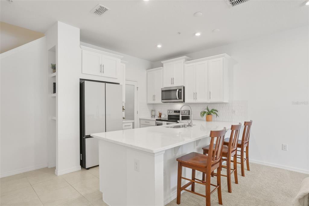 A modern kitchen features white cabinets, stainless steel appliances, a quartz island, and wooden bar stools — 10245 HIGHLINE CREST STREET, ORLANDO, FL