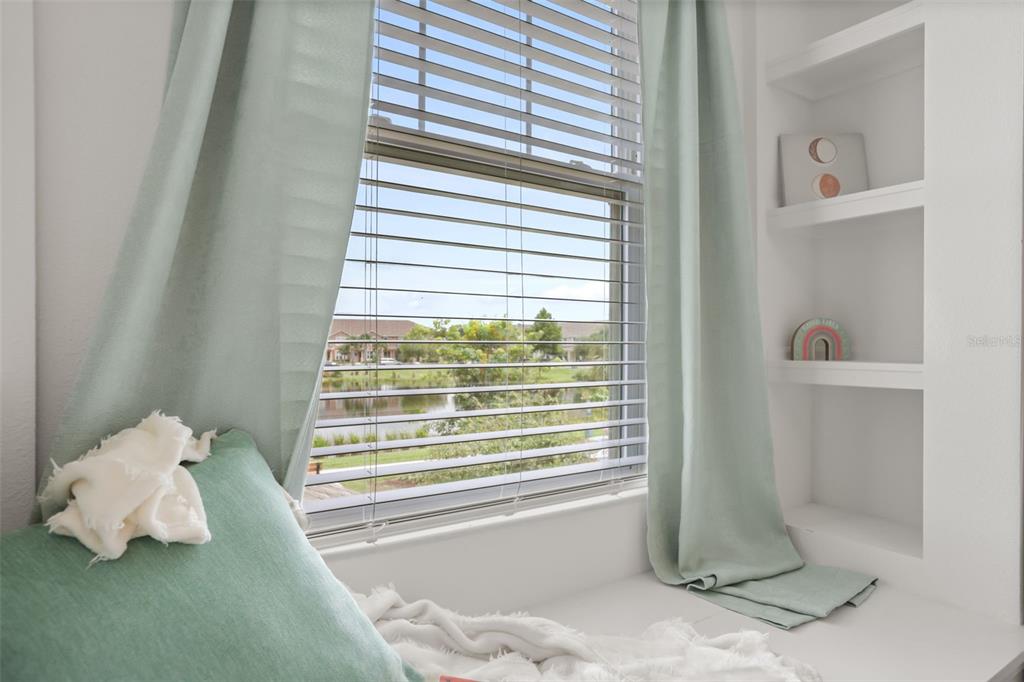 A window seat with light green curtains overlooks a pond and neighborhood homes — 10245 HIGHLINE CREST STREET, ORLANDO, FL