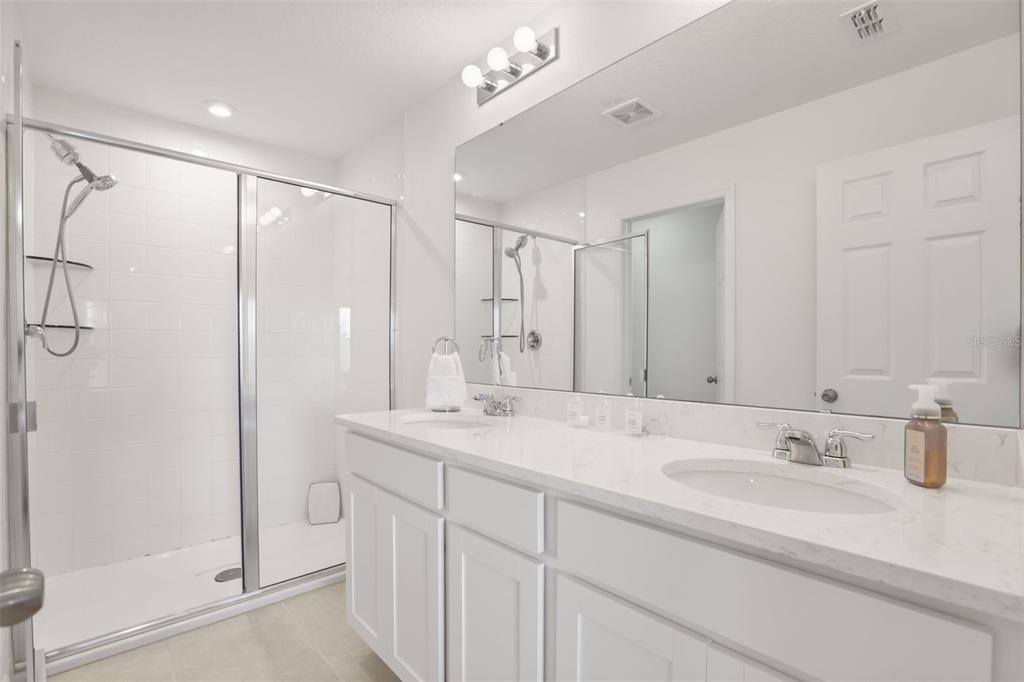 A modern bathroom features a double vanity with white cabinets, quartz countertops, and a glass-enclosed shower — 10245 HIGHLINE CREST STREET, ORLANDO, FL