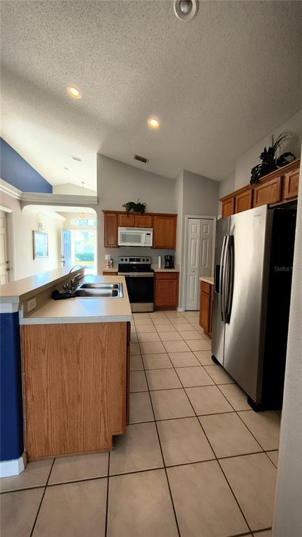 A kitchen features wood cabinets, stainless steel appliances, a tile floor, and a breakfast bar — 16721 S ROLLING GREEN DRIVE S, CLERMONT, FL