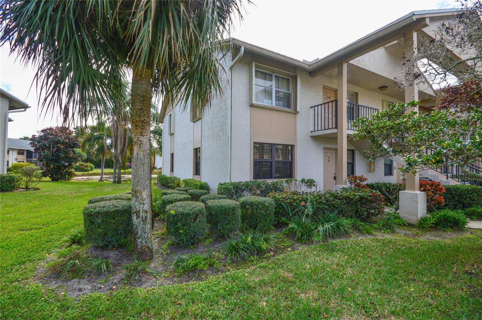 A two-story apartment building exterior features a palm tree, manicured shrubs, and a balcony — 3151 SE Aster Lane # 1301, Stuart FL 34994, STUART, FL