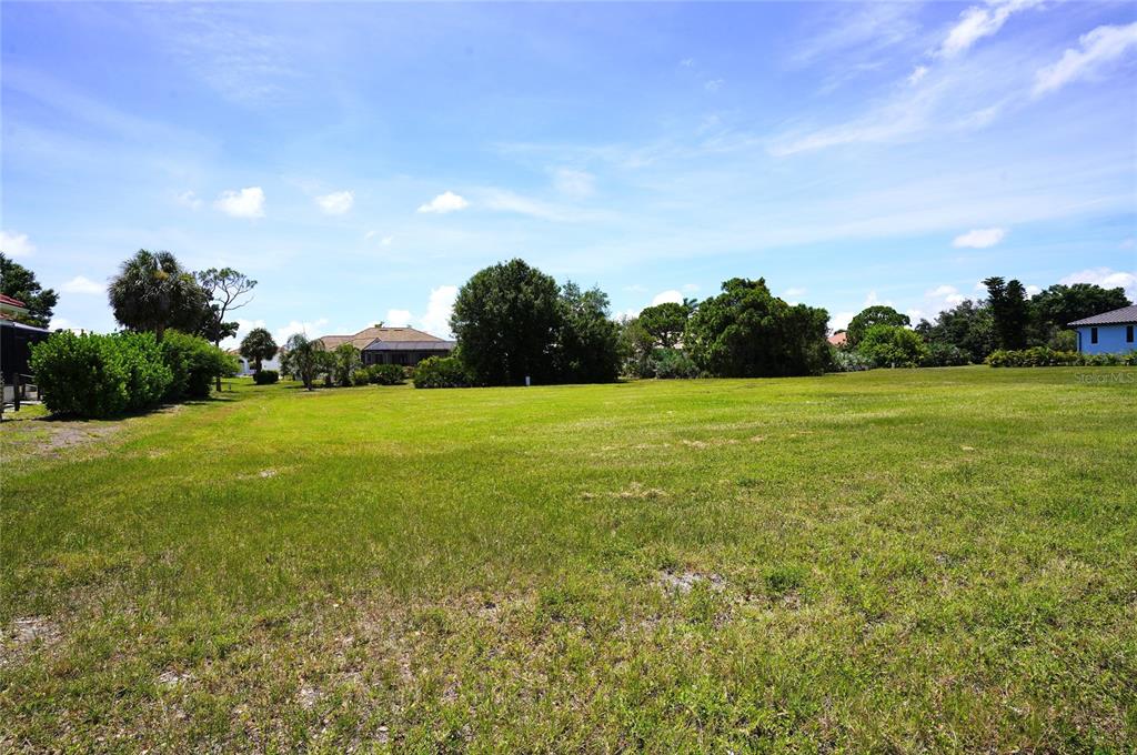 A large, flat, grassy vacant lot surrounded by trees and neighboring houses under a blue sky — 4250 CAPE HAZE DRIVE, PLACIDA, FL
