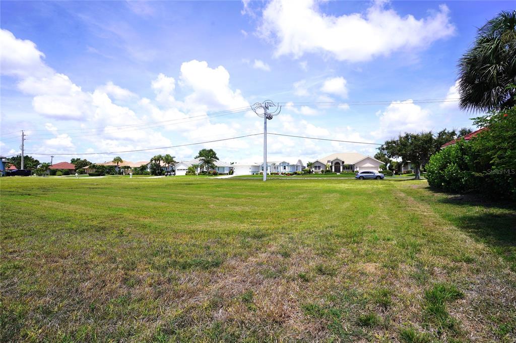A large, grassy vacant lot sits in front of several suburban houses under a cloudy sky — 4250 CAPE HAZE DRIVE, PLACIDA, FL