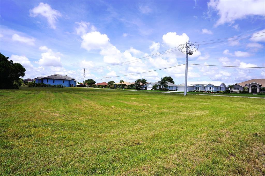 A large, grassy vacant lot sits in front of several suburban houses under a cloudy sky — 4250 CAPE HAZE DRIVE, PLACIDA, FL