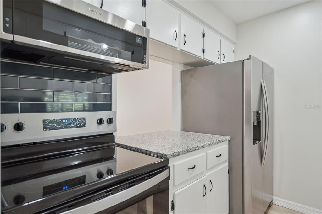 A kitchen features white cabinets, granite countertops, a stainless steel sink, and blue tile backsplash — 791 LAKE AVENUE UNIT 6, CLERMONT, FL