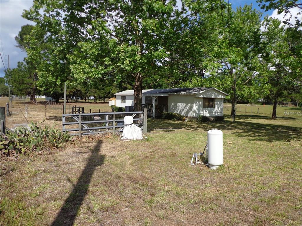 A white mobile home sits on a grassy lot behind a metal gate and trees — 17911 ORANGE DRIVE, SPRING HILL, FL