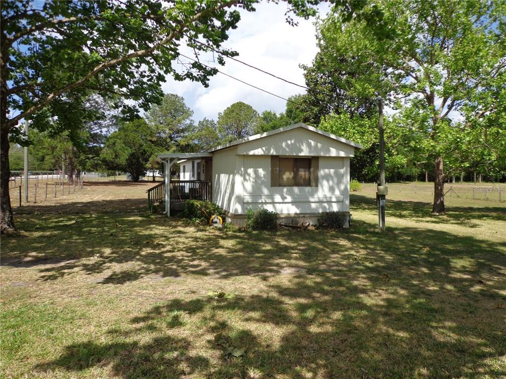 A single-story manufactured home sits on a grassy lot surrounded by mature trees — 17911 ORANGE DRIVE, SPRING HILL, FL