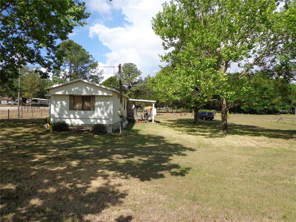 A single-story mobile home sits on a grassy lot with mature trees and a deck — 17911 ORANGE DRIVE, SPRING HILL, FL