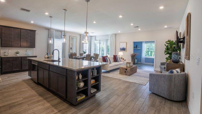 An open-concept kitchen and living area featuring dark cabinetry, a large island, and wood-look flooring — 17641 NW 168TH ROAD, ALACHUA, FL