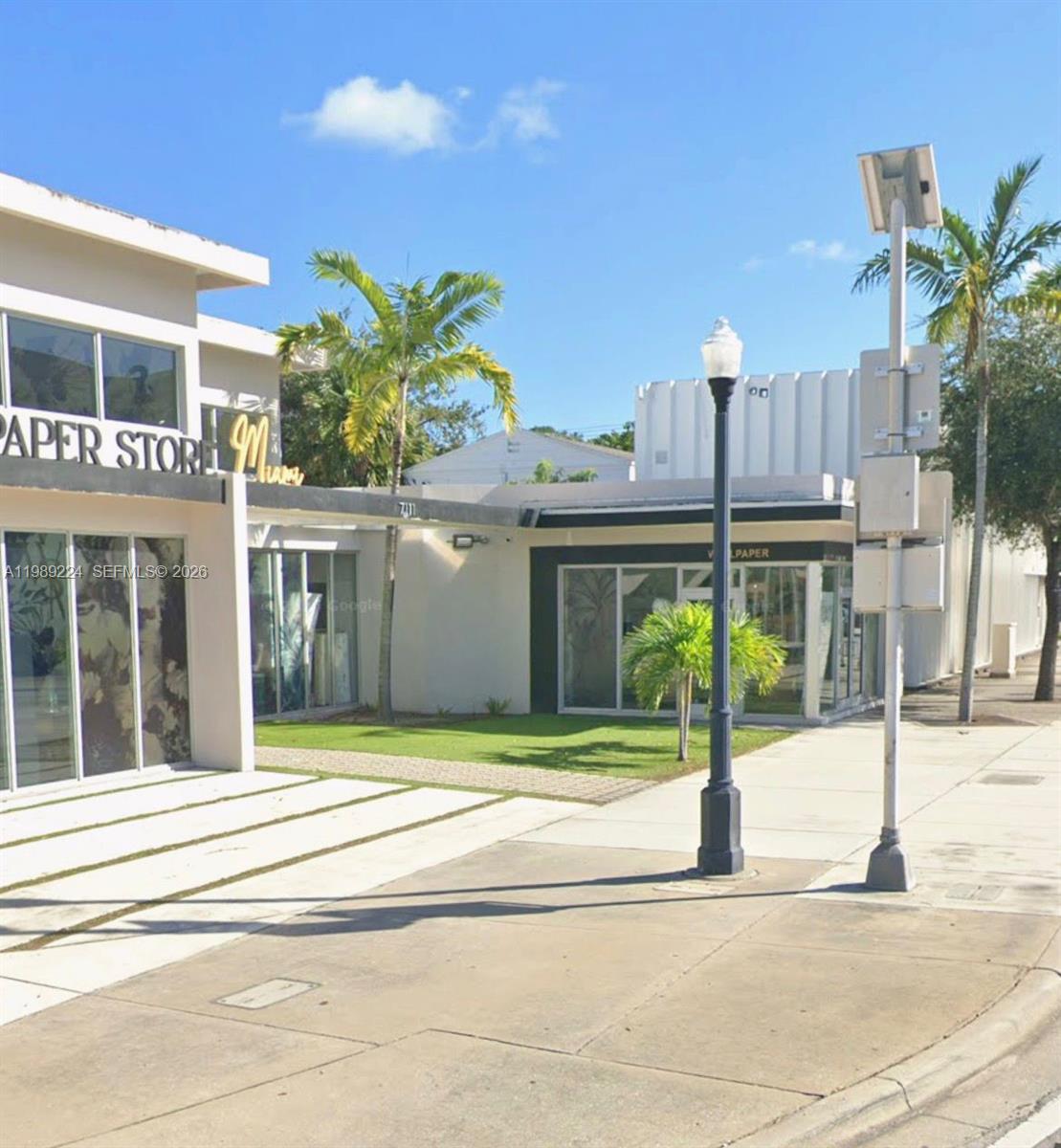 An exterior view of a commercial building with a storefront, palm trees, and sidewalk — 7111 Biscayne Blvd, Miami FL 33138, MIAMI, FL