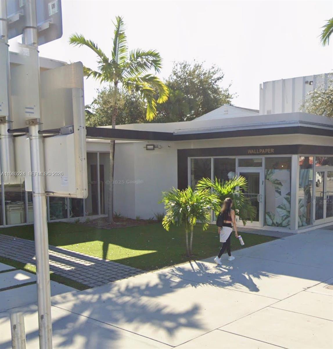 A person walks past a white commercial building with a glass storefront labeled wallpaper — 7111 Biscayne Blvd, Miami FL 33138, MIAMI, FL