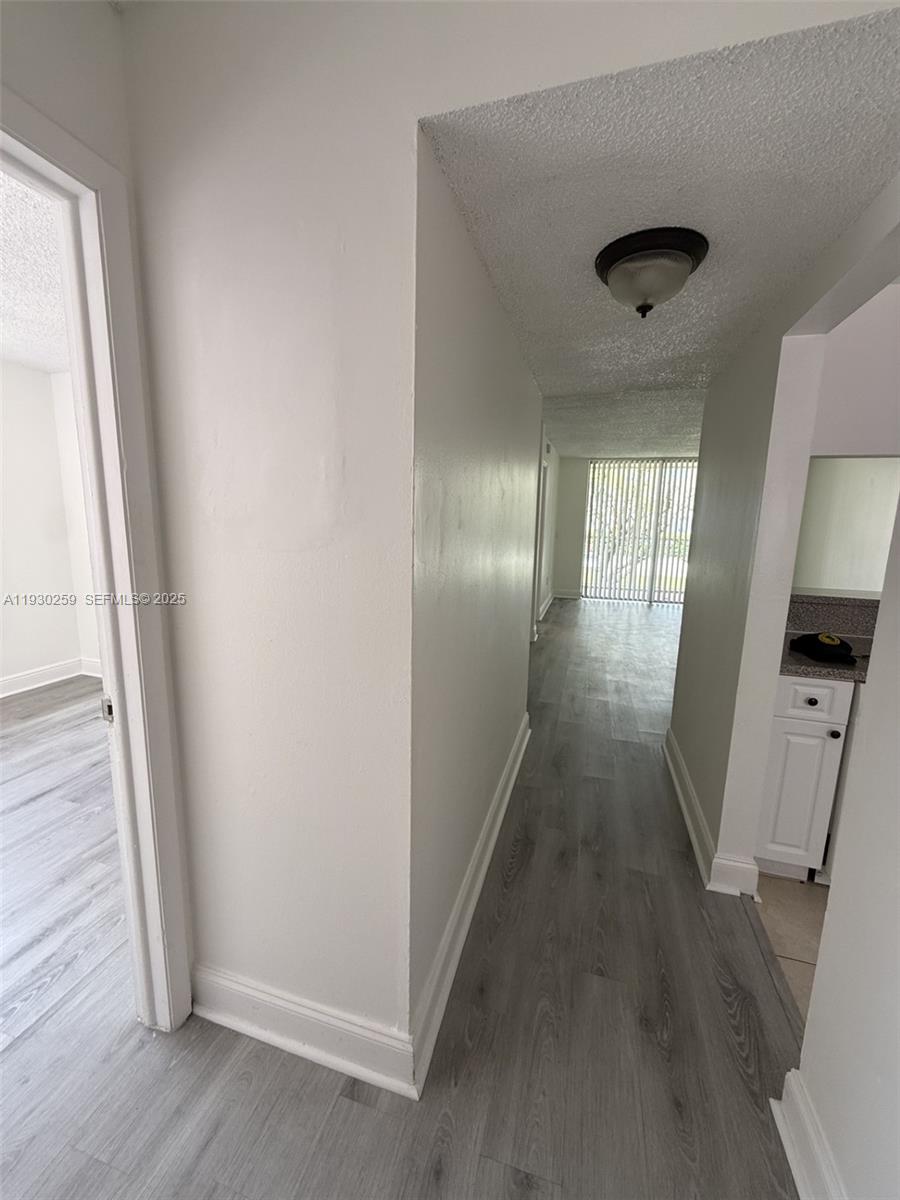 A hallway with gray wood-look flooring leads toward a room with sliding glass doors — 19729 SW 114th Ave # 251, Miami FL 33157, MIAMI, FL