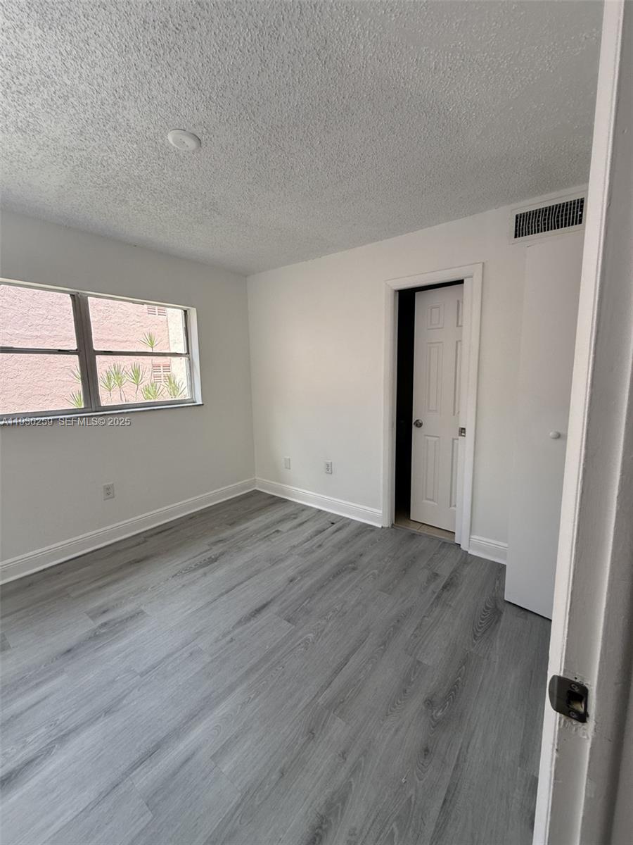 An empty bedroom features gray wood-look flooring, white walls, and a window overlooking a building — 19729 SW 114th Ave # 251, Miami FL 33157, MIAMI, FL