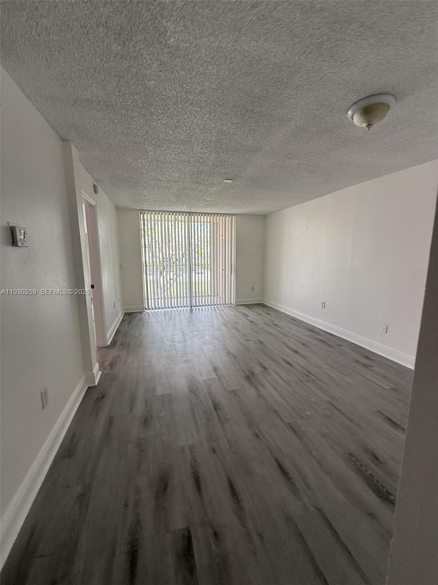 An empty living room features gray wood-look flooring, white walls, and vertical window blinds — 19729 SW 114th Ave # 251, Miami FL 33157, MIAMI, FL