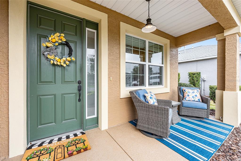 A covered front porch features a green door, two wicker chairs, and a striped rug — 8566 SW 79TH AVENUE, OCALA, FL
