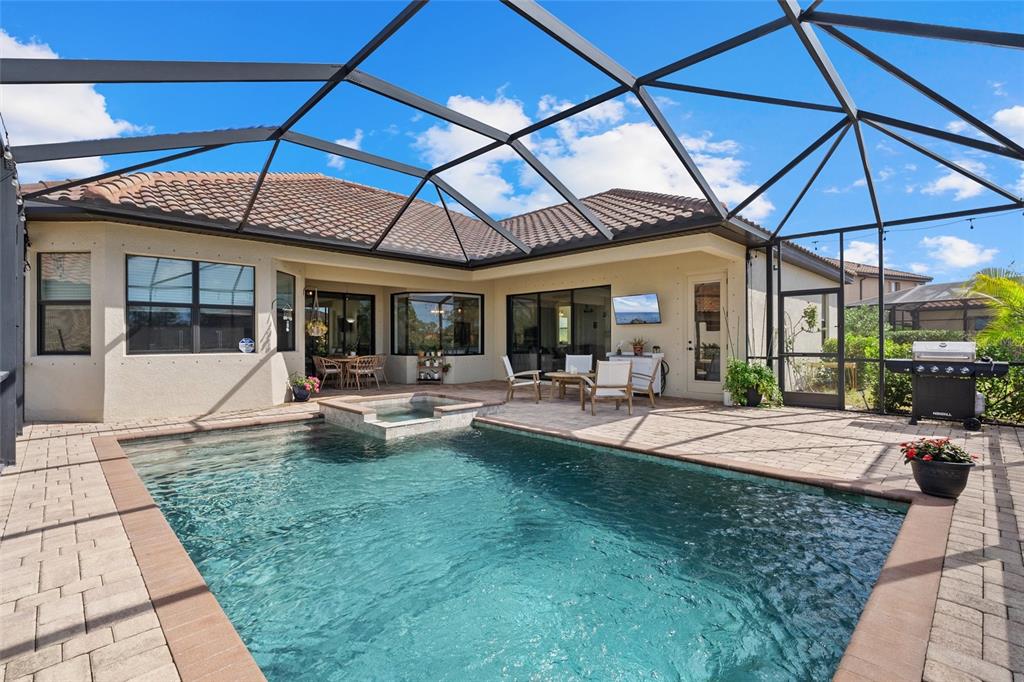A swimming pool and spa are enclosed by a screened lanai behind a house — 20655 VALPRATO COURT, VENICE, FL