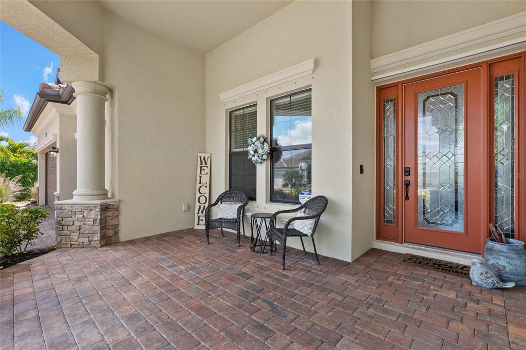 A covered front porch features brick pavers, two wicker chairs, and a reddish-brown front door — 20655 VALPRATO COURT, VENICE, FL
