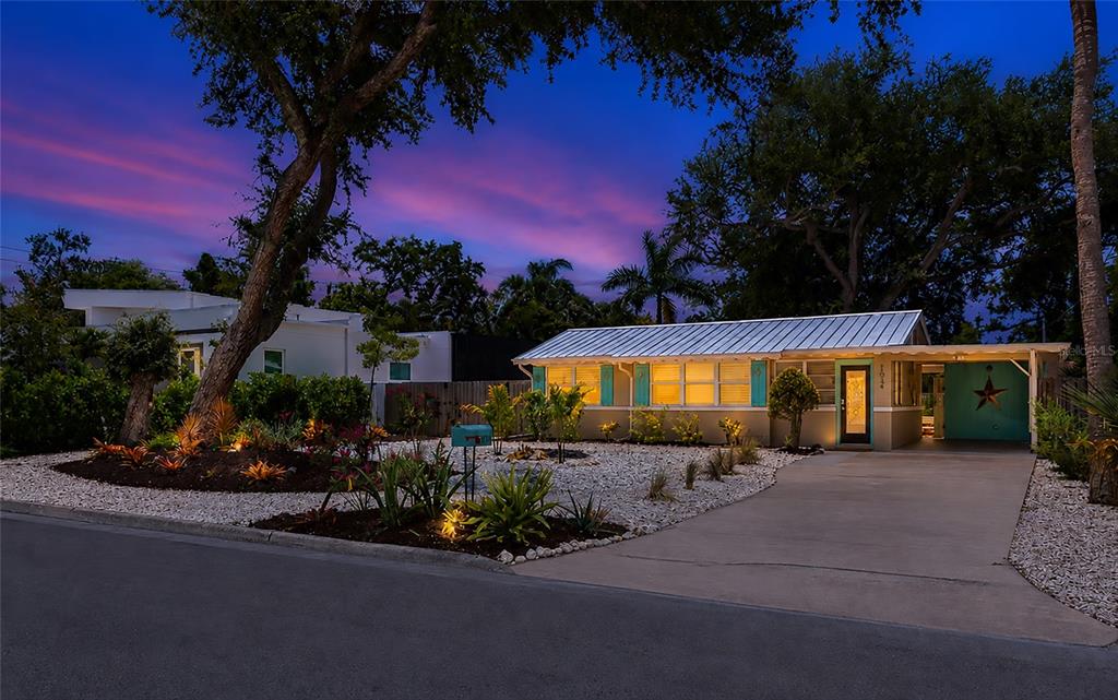 A single-story house with a metal roof, turquoise door, and gravel landscaping at dusk — 1034 N 22ND STREET, SARASOTA, FL