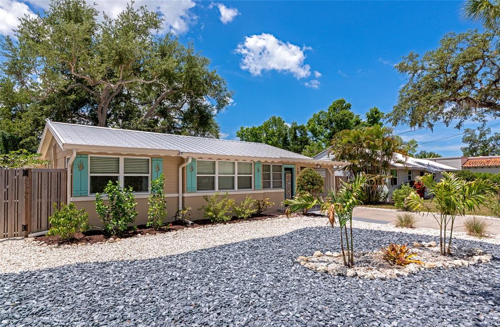 A single-story house with a metal roof, light siding, and turquoise shutters sits behind gravel — 1034 N 22ND STREET, SARASOTA, FL