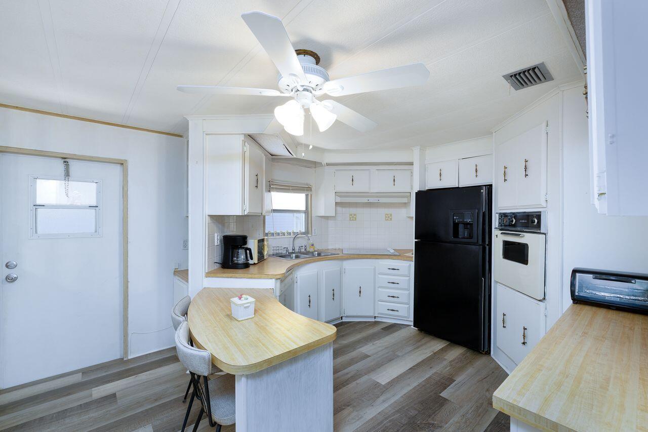 A kitchen with white cabinets, a black refrigerator, wood-look flooring, and a small breakfast bar — 2001 N 83rd Ave Avenue N # 1281, FL 33702, FL