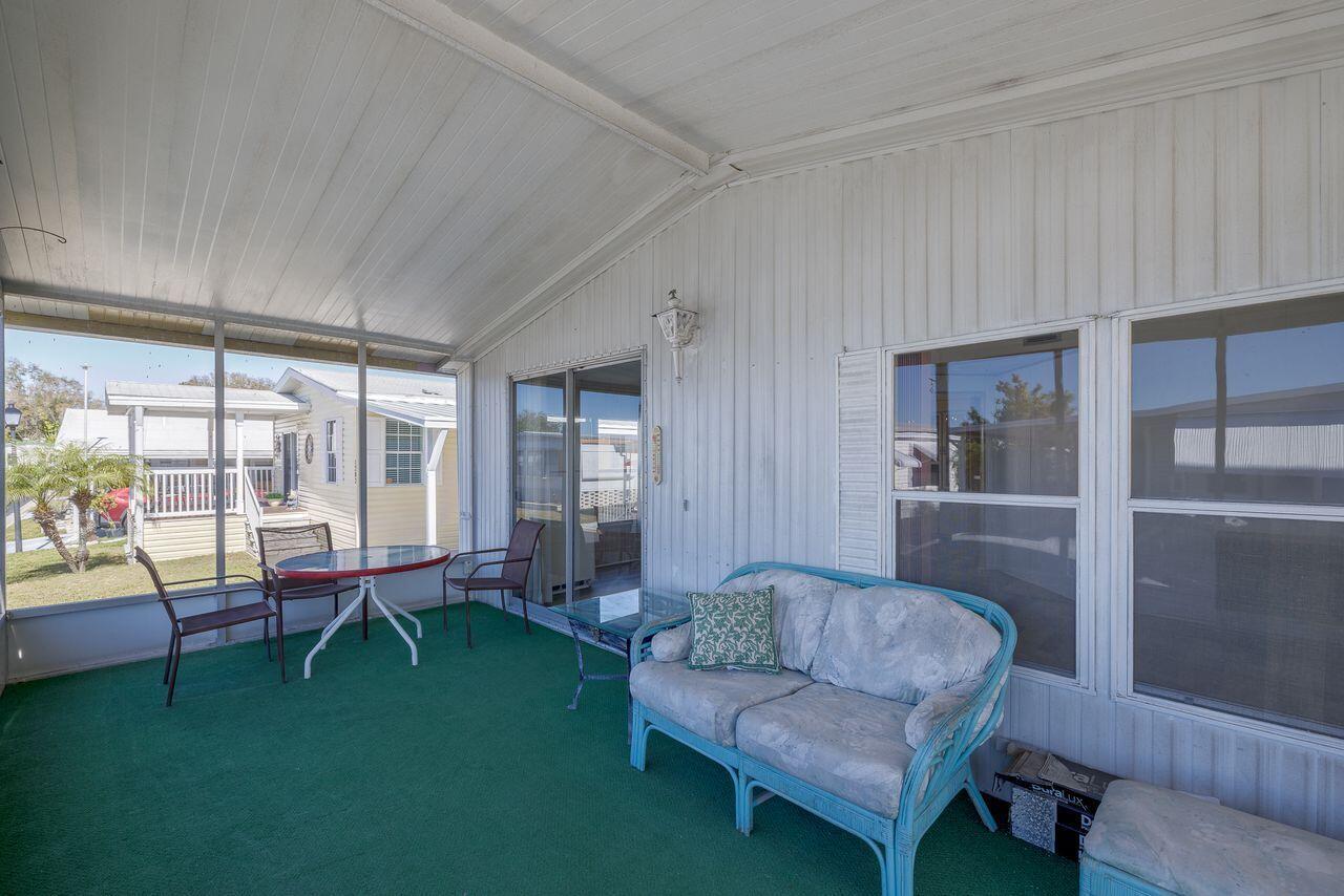A screened-in porch features green carpeting, a blue wicker loveseat, and a small dining set — 2001 N 83rd Ave Avenue N # 1281, FL 33702, FL