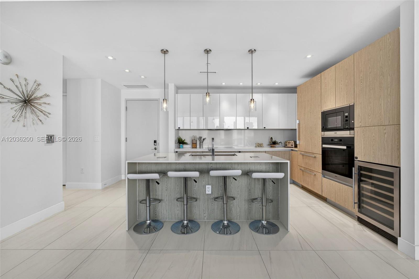 A modern kitchen features a central island with four stools, white cabinets, and wood-paneled appliances — 3100 N Ocean Dr # 1801, Singer Island FL 33404, SINGER ISLAND, FL