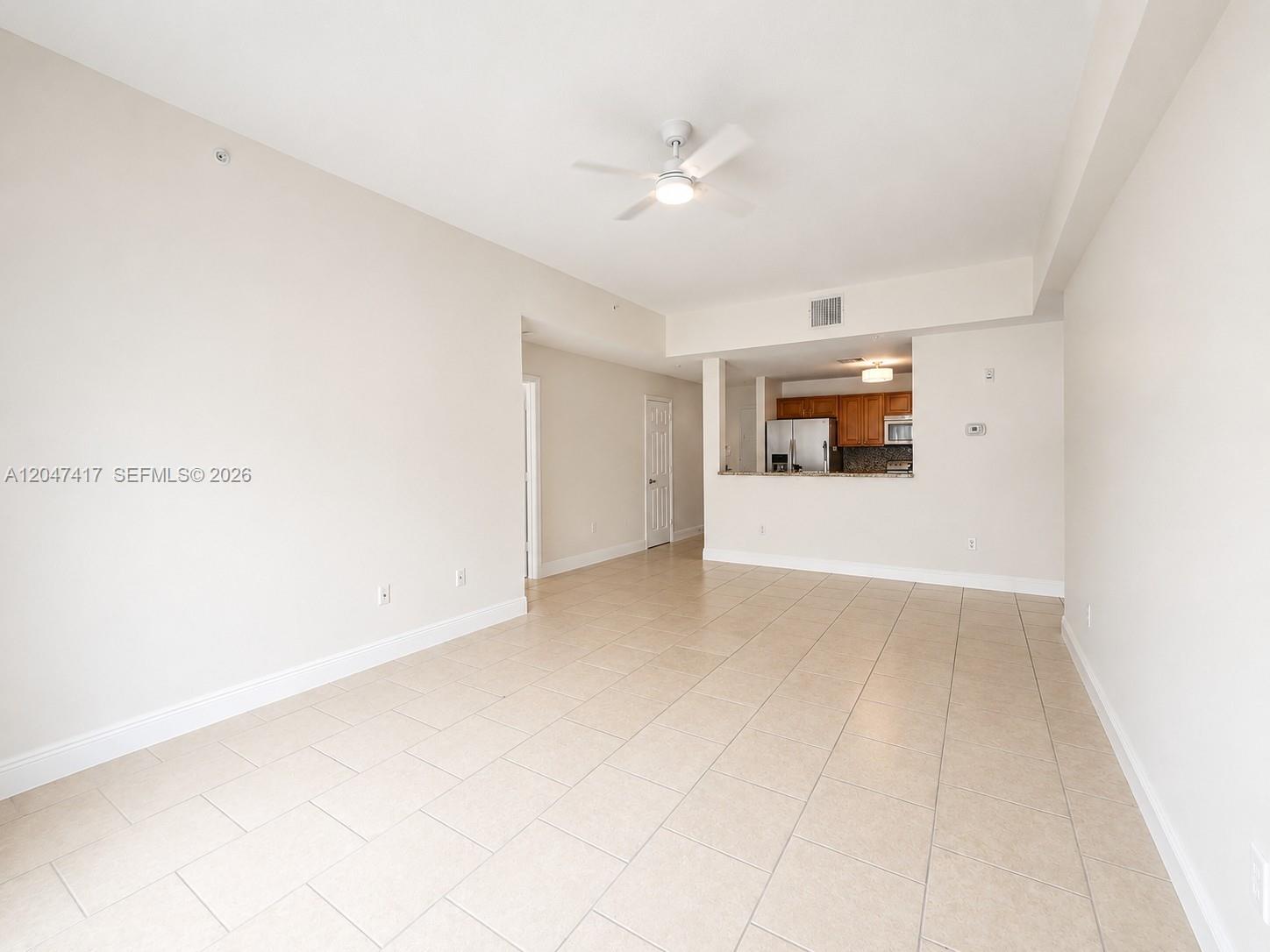An empty living room with beige tile flooring features a ceiling fan and an open kitchen — 1203 Town Center # 314, Jupiter FL 33458, JUPITER, FL