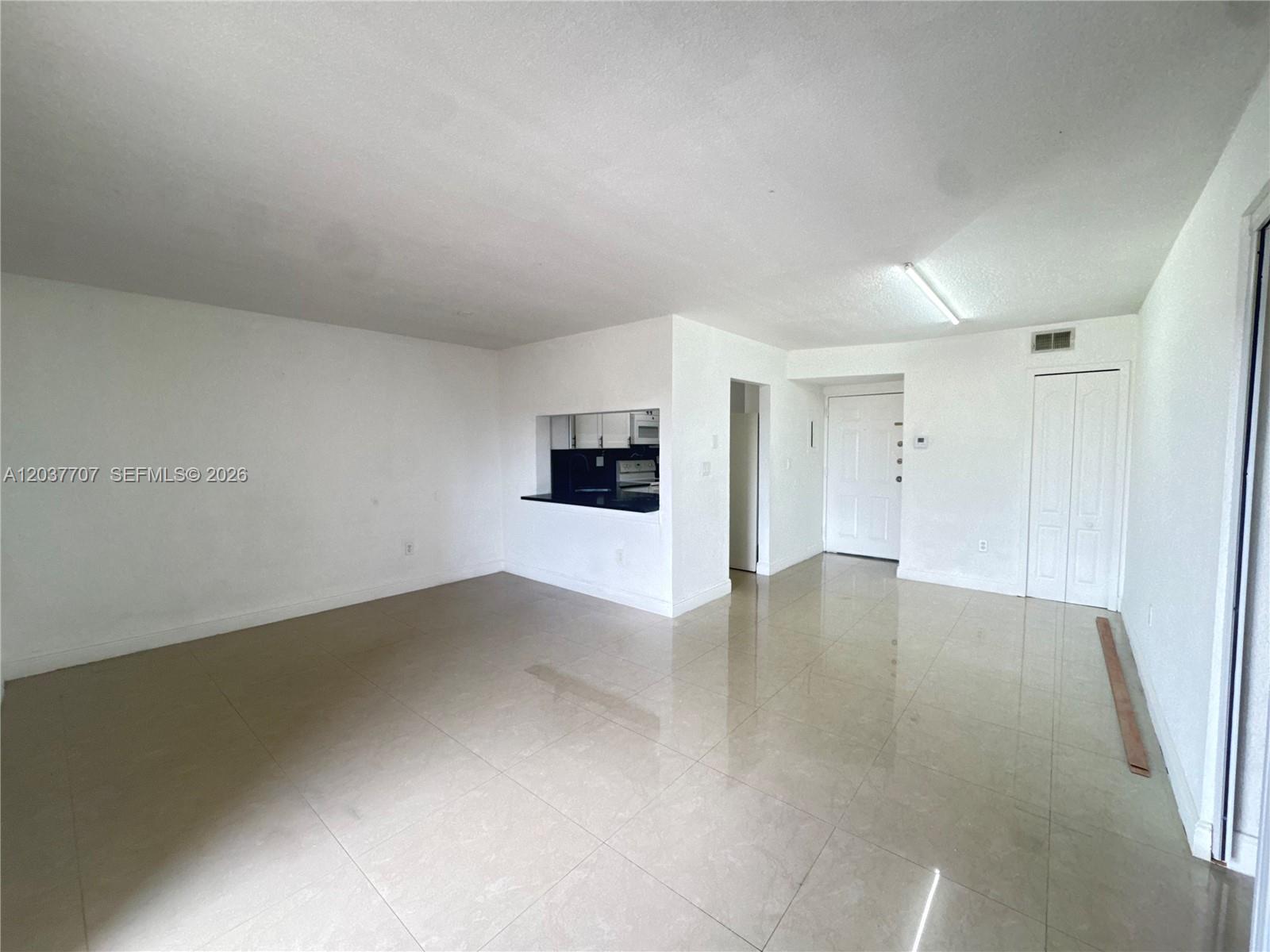 An empty living area features white walls, beige tile flooring, and a kitchen pass-through window — 8500 NW 8th St # 303, Miami FL 33126, MIAMI, FL