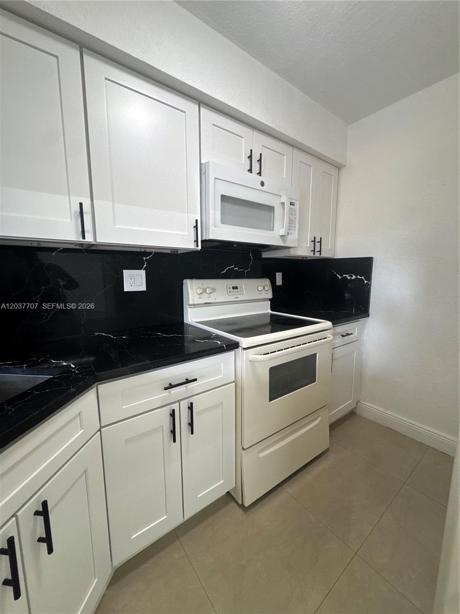 A kitchen features white cabinets, black marble-patterned countertops, and a white stove and microwave — 8500 NW 8th St # 303, Miami FL 33126, MIAMI, FL