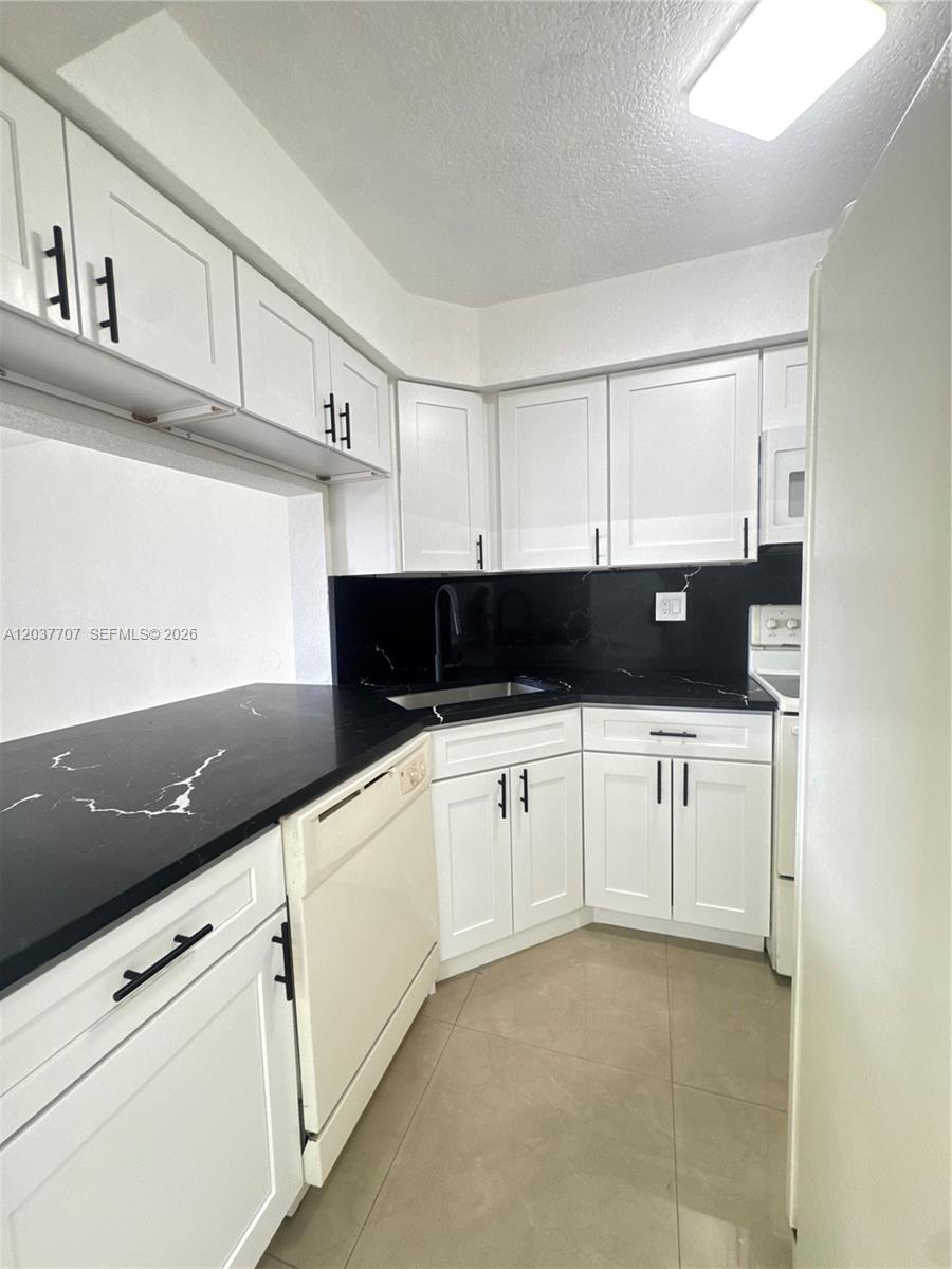 A kitchen features white cabinets, black countertops, and light-colored tile flooring — 8500 NW 8th St # 303, Miami FL 33126, MIAMI, FL