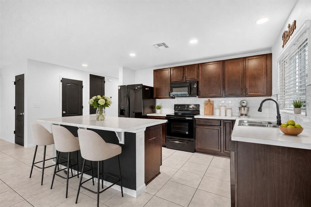 A kitchen with dark wood cabinets, a central island with bar seating, and white countertops — 1097 AUGUSTUS DRIVE, DAVENPORT, FL