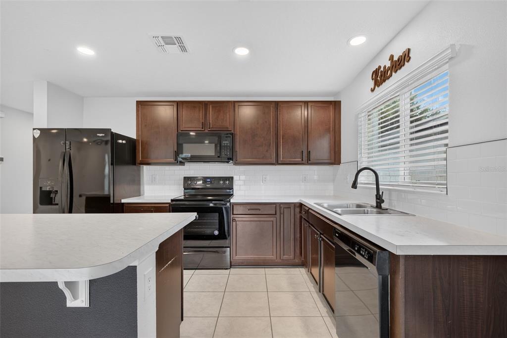 A kitchen features dark wood cabinets, white countertops, a subway tile backsplash, and black appliances — 1097 AUGUSTUS DRIVE, DAVENPORT, FL