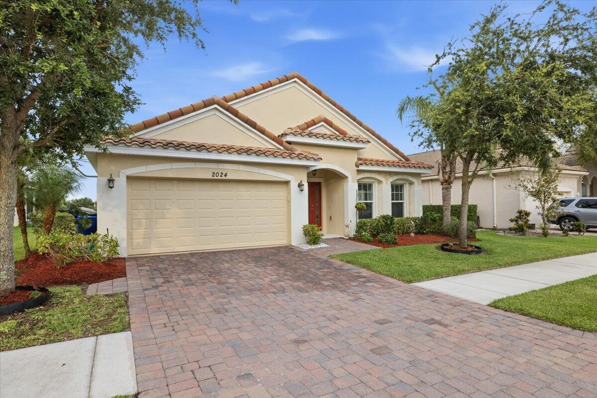 A single-story house with a beige stucco exterior, a two-car garage, and a brick driveway — 2024 Albany Terrace SW, Vero Beach FL 32968, VERO BEACH, FL