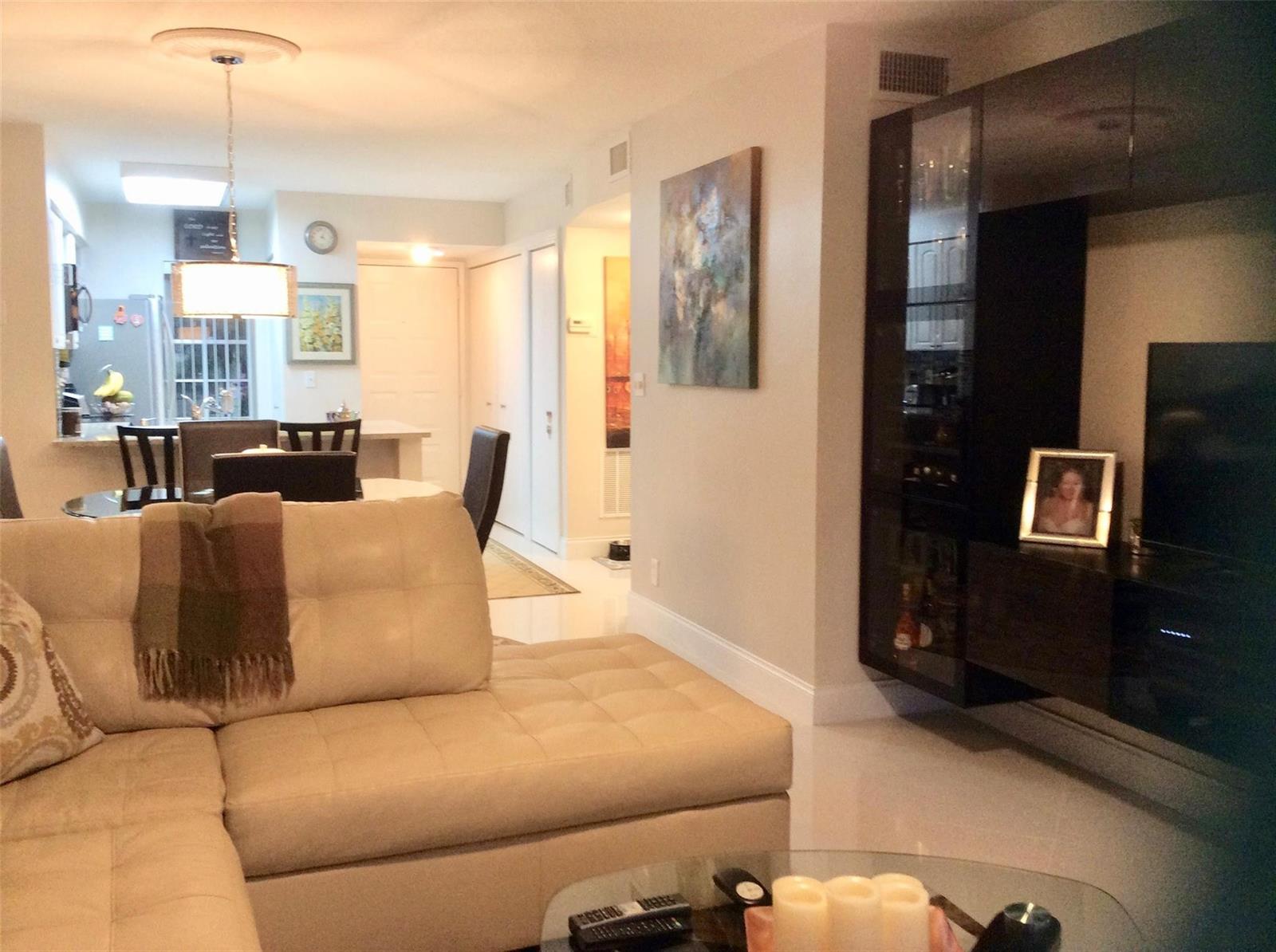 A living room with a beige sectional sofa, glass coffee table, and dark wall unit — 2220 N Cypress Bend Drive # 104, Pompano Beach FL 33069, POMPANO BEACH, FL