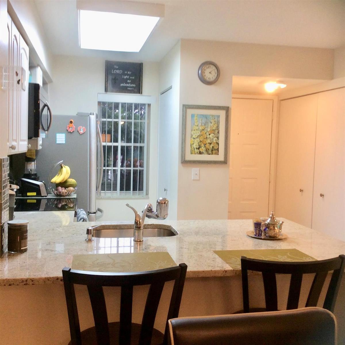 A kitchen features a granite-topped island, a stainless steel sink, and white cabinetry — 2220 N Cypress Bend Drive # 104, Pompano Beach FL 33069, POMPANO BEACH, FL