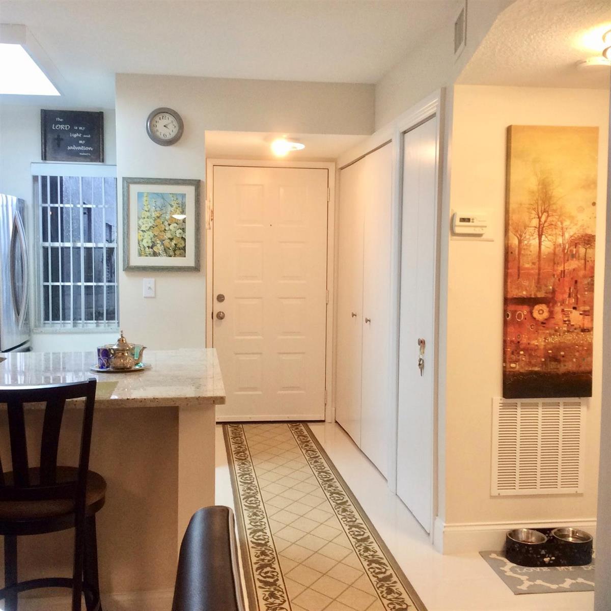 An entryway features a white door, a long patterned runner, and a granite-topped kitchen island — 2220 N Cypress Bend Drive # 104, Pompano Beach FL 33069, POMPANO BEACH, FL
