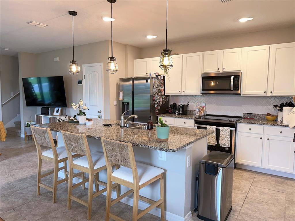 A kitchen features a granite-topped island with three wooden stools and white cabinetry — 10126 SALT POINT DRIVE, WINTER GARDEN, FL