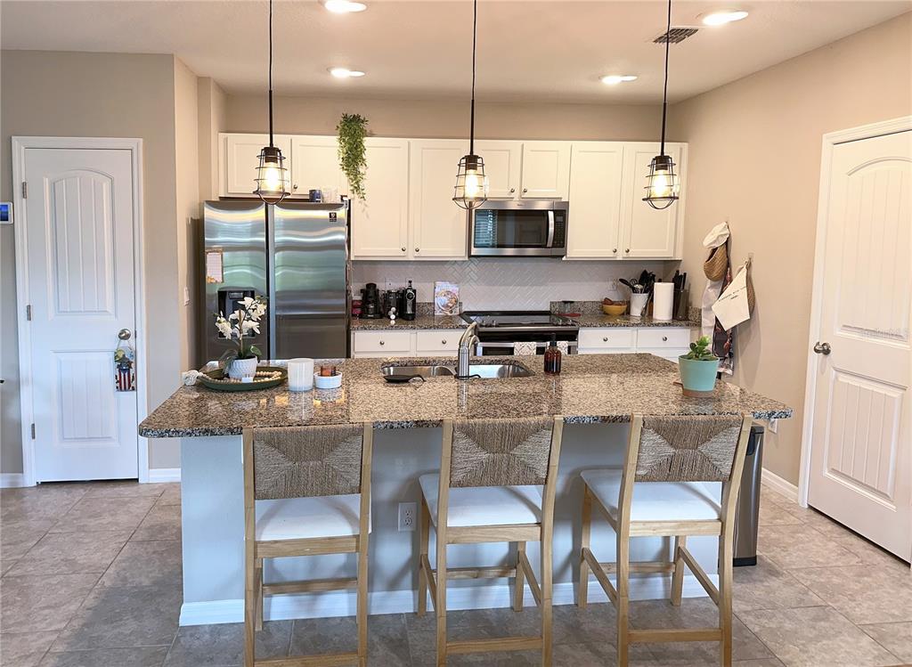 A kitchen features white cabinets, granite countertops, a central island with seating, and stainless appliances — 10126 SALT POINT DRIVE, WINTER GARDEN, FL